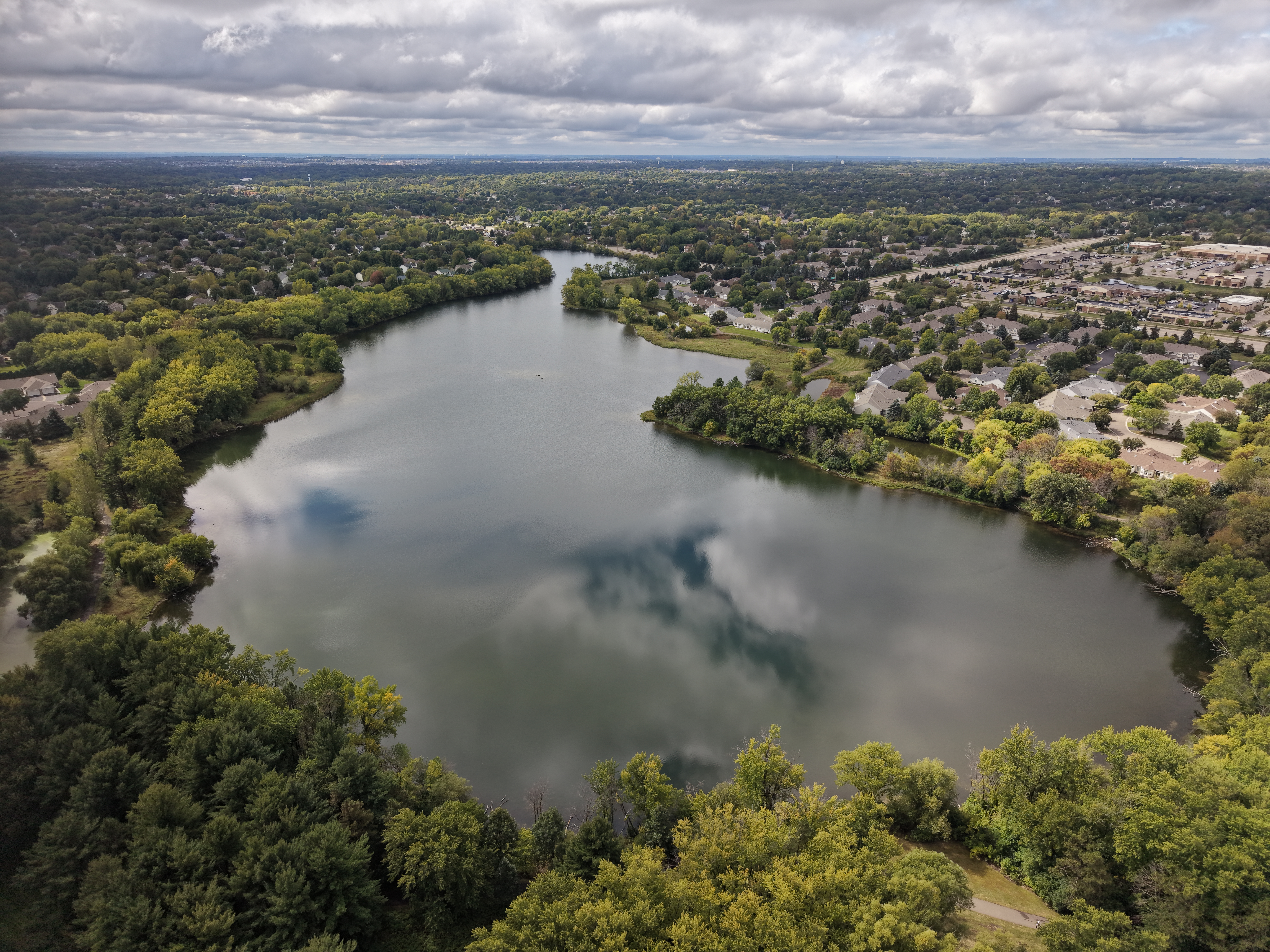 Aerial image of a dark blue lake among green trees in a suburban area