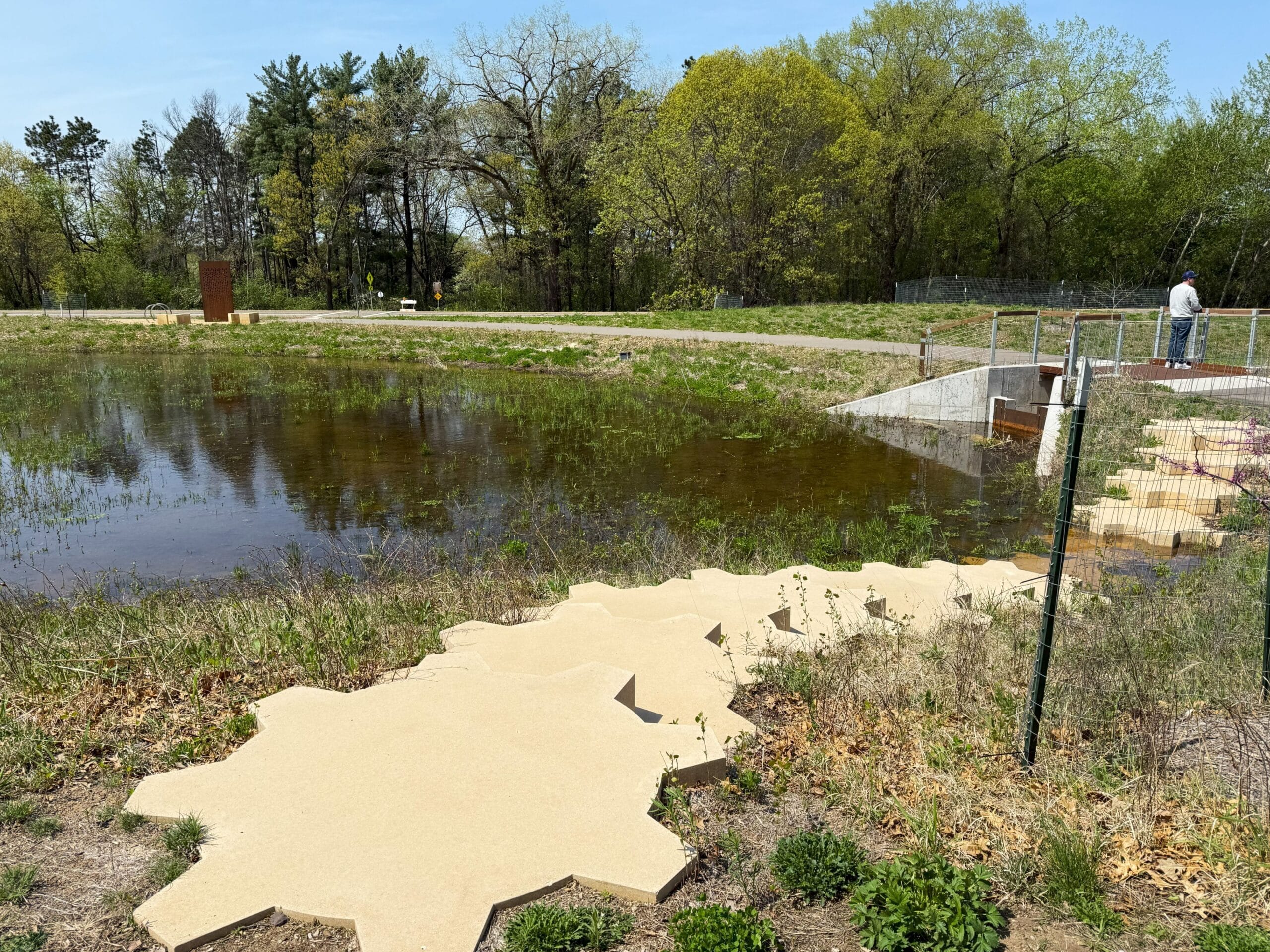 Large sculptural gears positioned as stairs from the sidewalk and into a pond