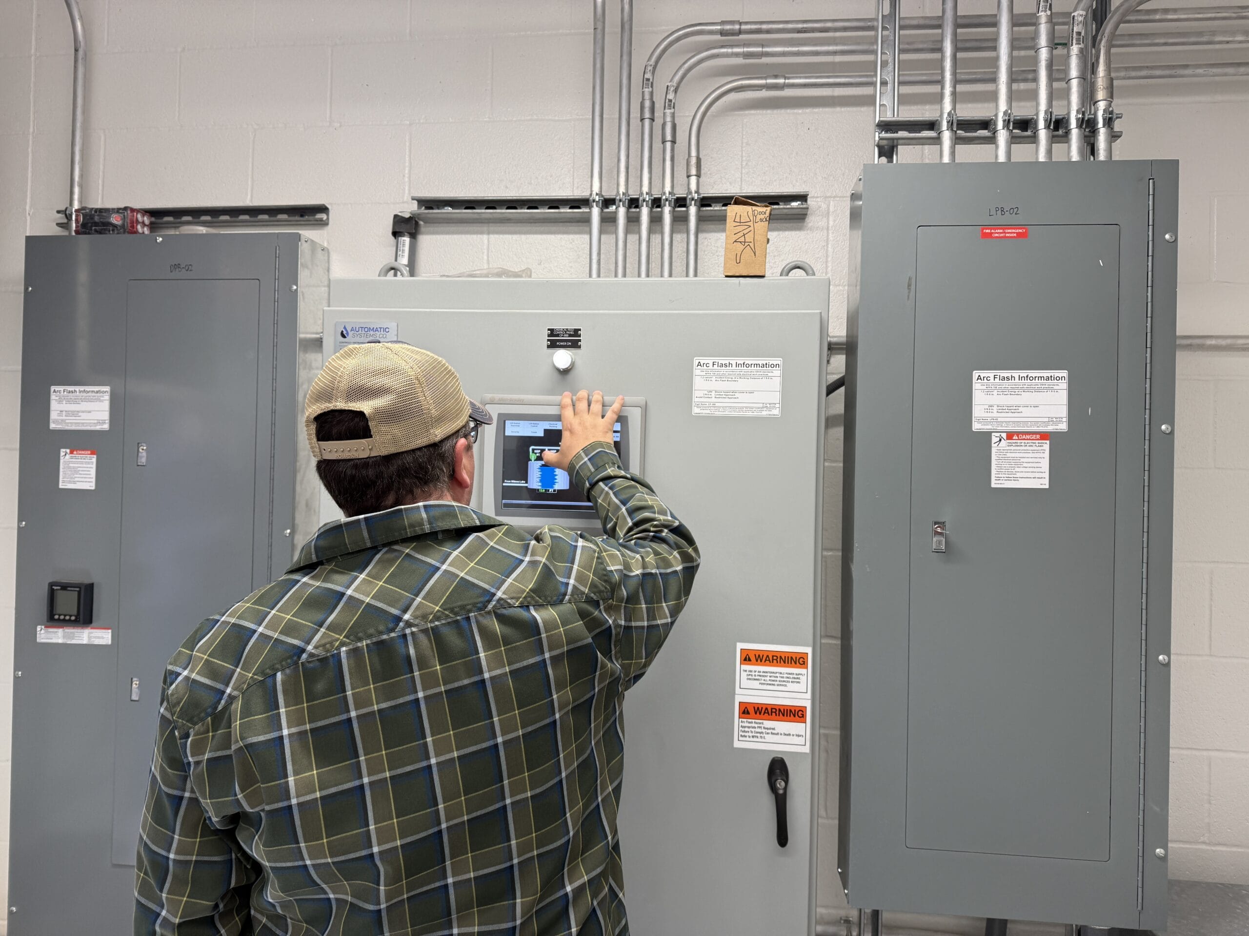 A person stands in front of a electrical panel and interacts with a touch screen