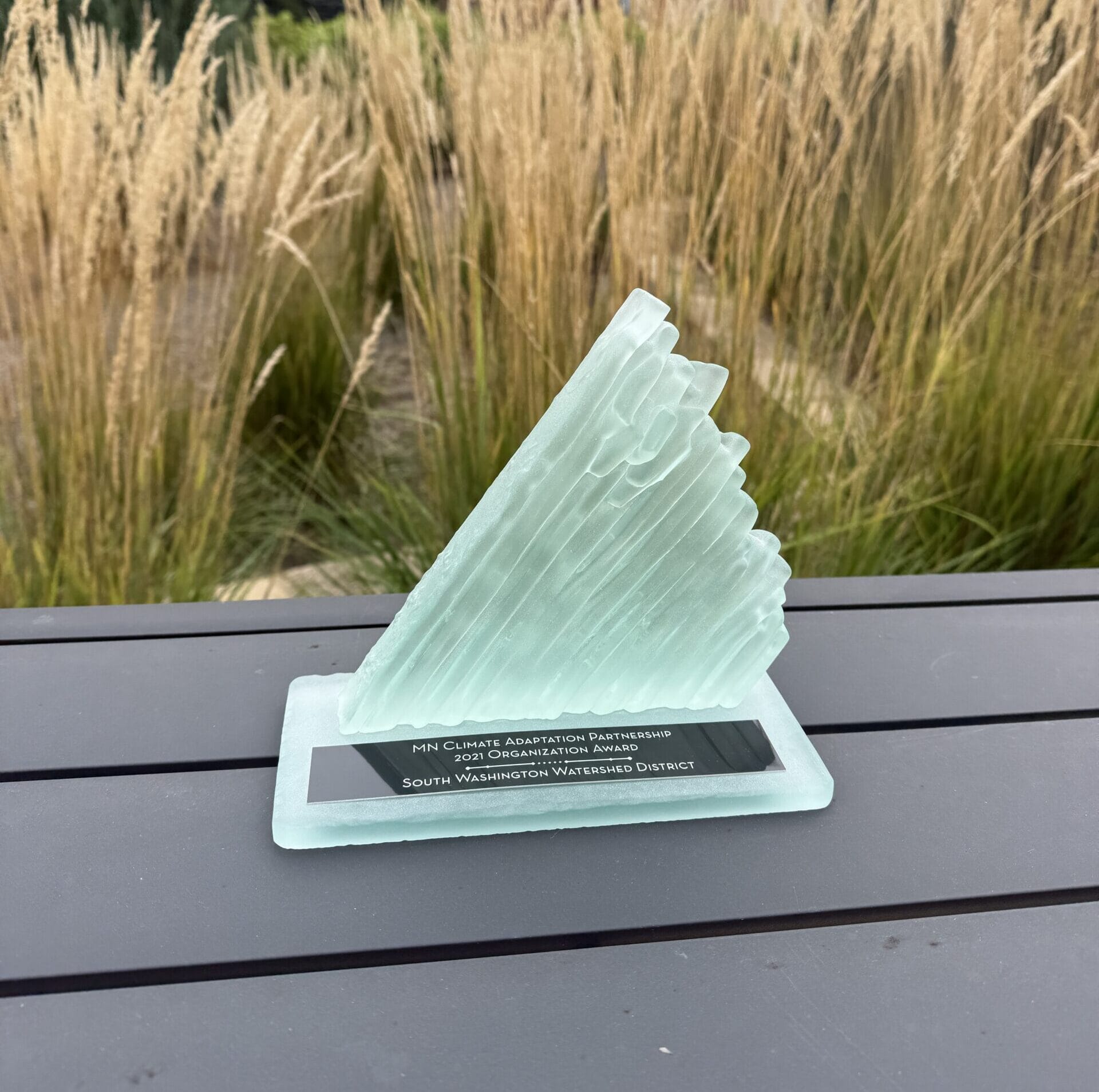 Abstract piece of glass in the shape of a iceberg placed on top of another piece of glass with a plaque reading "MN Climate Adaptation Partnership 2021 Organization Award: South Washington Watershed District"