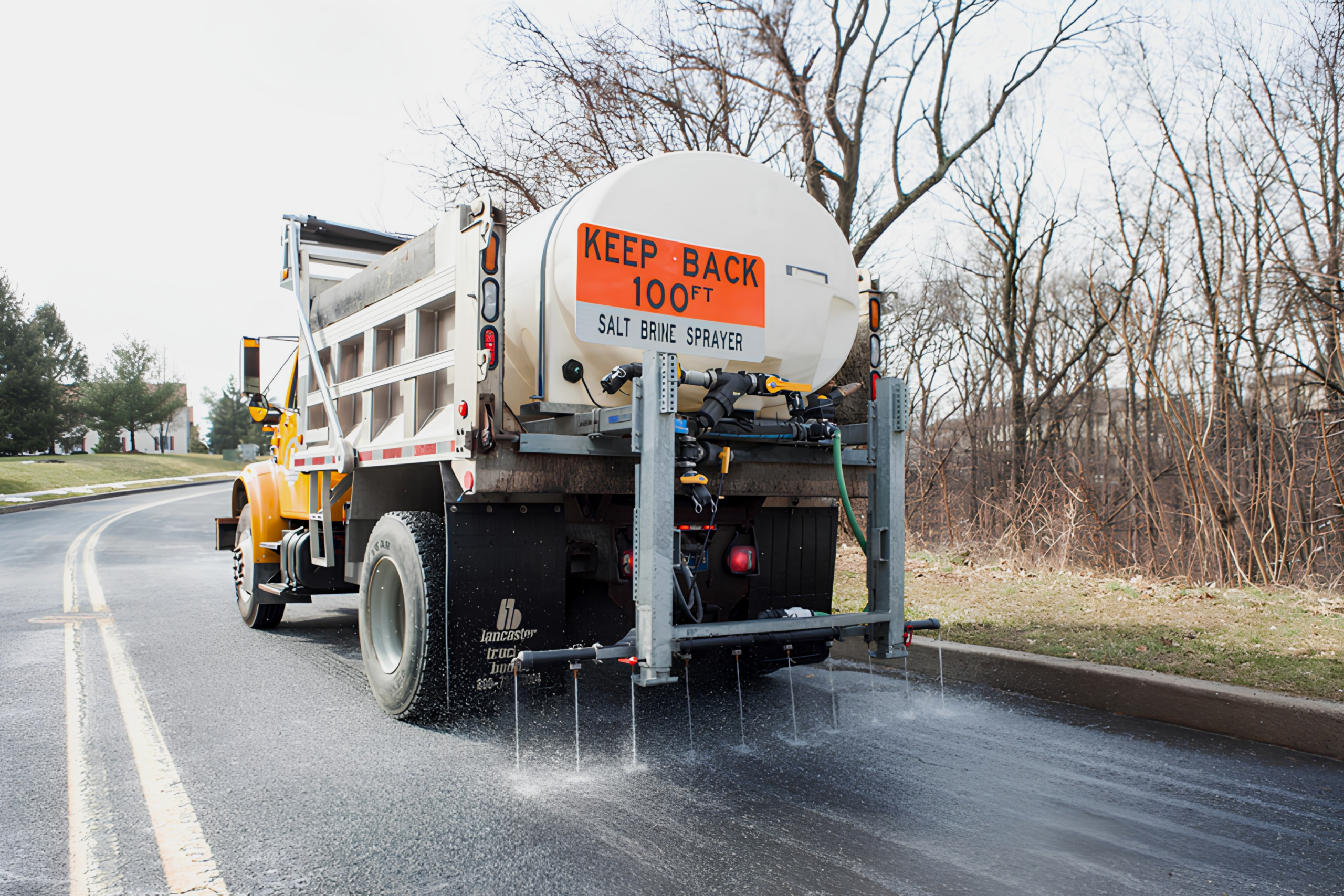 A large truck driving down a suburban road dispensing brine solution in stripes