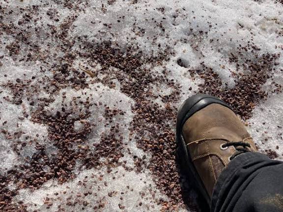 Small rocks on a snowy ground with a adult foot in a winter boot