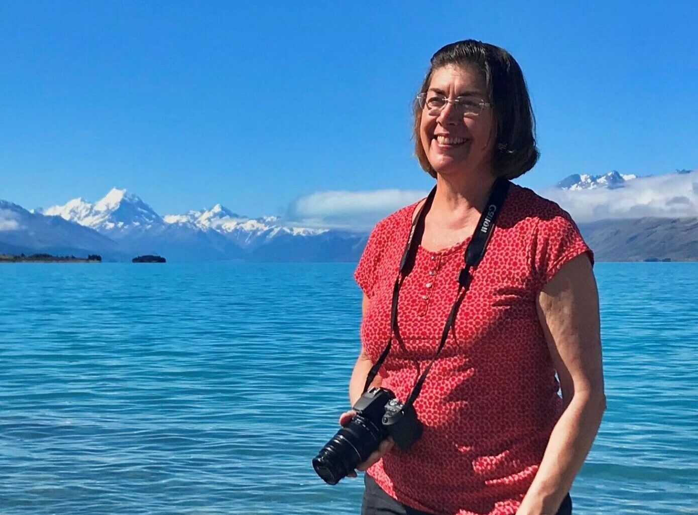 Adult woman standing on rocky shore with a camera hanging on a strap around the neck